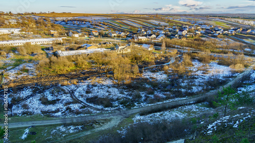 Top view aerial rural countryside winter or early spring landscape. Dirt road  village houses and riever. Fields covered by young green grass and snow. Copy space long image background.
