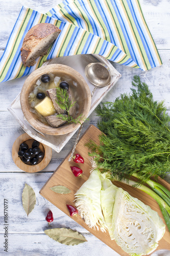 traditional soup of fresh cabbage and pulp of beef with potatoes, in a wooden bowl on a white background. Nearby is a half-a-half of different colors. Olives and green dill, fresh cabbage and red pepp photo