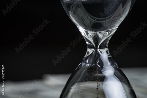 Fotografie Closed up of sandglass or hourglass with reflection of US dollar banknotes on bl
