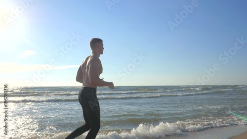 Running fit man jogging on beach. Side view