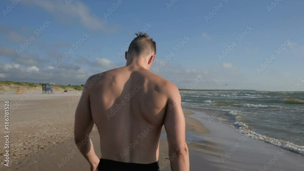 Wet athletic body muscular man walking on beach Wet athletic body muscular man walking on beach