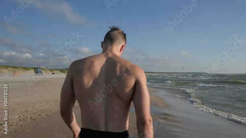 Wet athletic body muscular man walking on beach