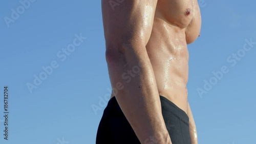 Man fitness model posing on beach outdoors.