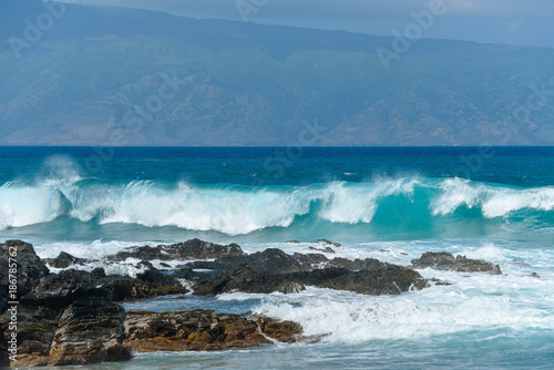 Breaking Waves - Big breaking blue waves rushing towards black rocky coast  with a tropical island in the background. Maui  Hawaii  USA.