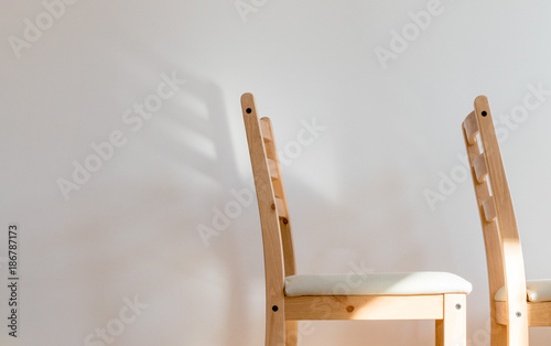 Chair dreaming of wings; two wooden chairs before a clean white wall, the back of one of casts a wing-shaped shadow