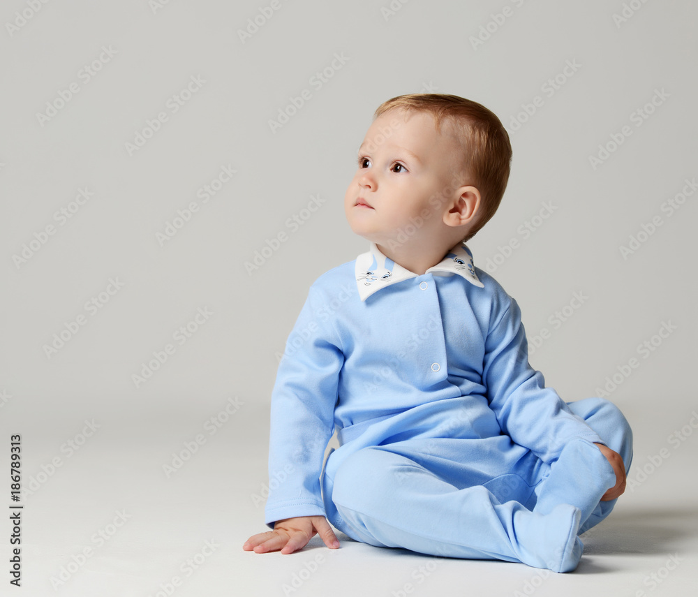 Infant child baby boy kid toddler sitting in light blue body cloth looking at the corner Infant child baby boy kid toddler sitting in light blue body cloth looking at the corner