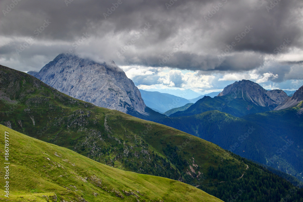 Green hills and rocky ridges of Carnic Alps with towering giant limestone Monte Peralba Hochweissstein peak capped with dark low storm clouds Veneto / Friuli Venezia Giulia Northern Italy Europe