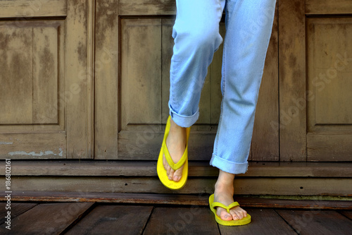 Yellow Flip Flops. Woman Legs and Feet Wearing Yellow Sandals Standing on Wooden Floor and wooden Wall Background Great for Any Use.
