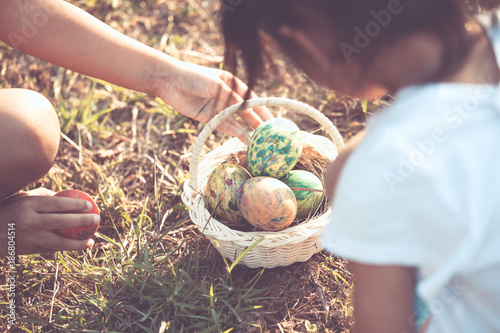 Two asian child girls playing and collecting colorful Easter eggs in basket together in outdoor in vintage color tone