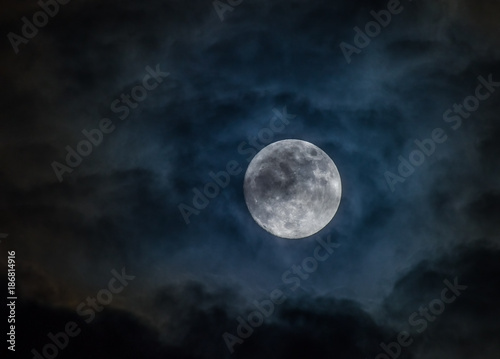Super full Moon shining through dark clouds