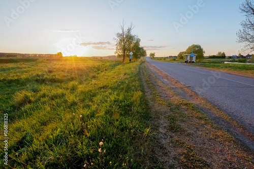 Rural road in the village next to the field at sunset