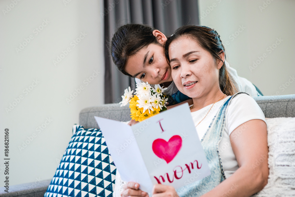 Mom and daughter reading a greeting card together happily in family's home on mother's day Festival.