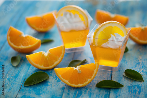 Orange jelly in a cup with whipped cream and orange sliced on blue wooden  background