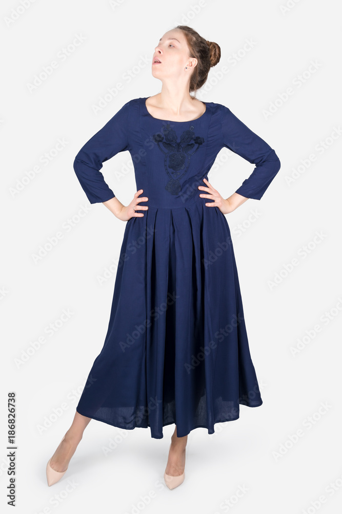 Female model wearing dress posing on grey neutral background. Beauty stylish woman proposing product, advertising gesture. Fashionable clothes in studio.