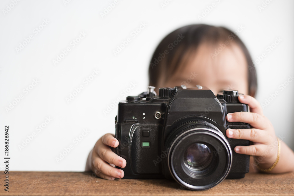 little asian toddler playing with old film camera (dslr). learning concept
