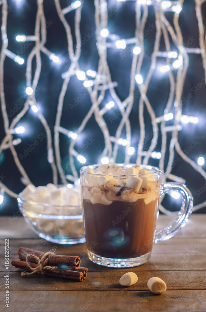 Hot chocolate, cinnamon sticks and marshmallow on the background of burning garlands, Christmas decorations, close up Hot chocolate, cinnamon sticks and marshmallow on the background of burning garlands, Christmas decorations, close up