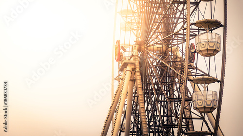 Close up view of the gondolas suspended from the rim of a ferris wheel lit by the warm glow of the sun at an amusement park with copy space