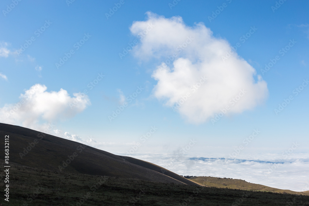 View of Subasio mountain (Umbria) over valley filled by fog, and beneath a wide sky with white clouds View of Subasio mountain (Umbria) over valley filled by fog, and beneath a wide sky with white clouds