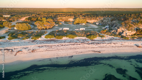 Aerial view of four wheel drive vehicles and caravans at a free camp next to a beach and cliffs in the late afternoon photo