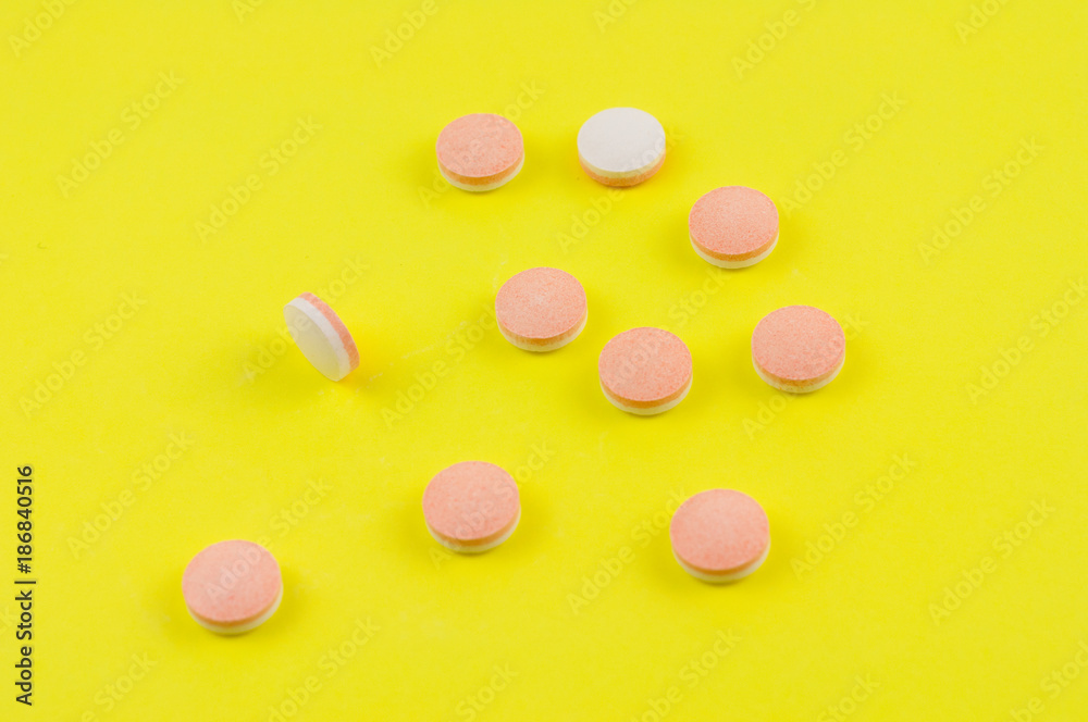 Scattered whole white and pink pills on background of yellow paper Scattered whole white and pink pills on background of yellow paper