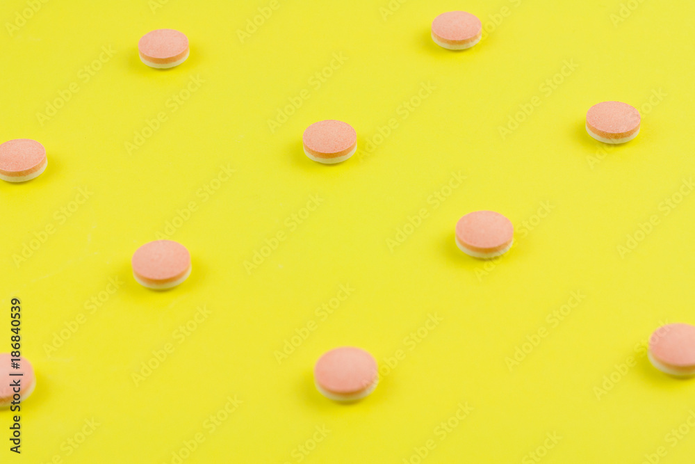 Scattered whole white and pink pills on background of yellow paper