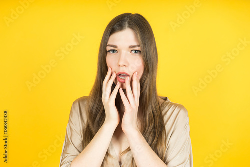Portrait of surprised beautiful girl holding her head in amazement and open-mouthed. Over yellow background.