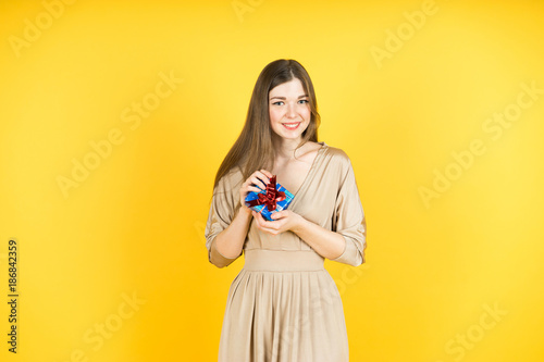 Portrait of casual young happy smiling woman hold small gift box. Isolated studio yellow background female model.