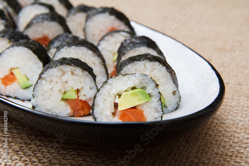 Sushi rolls in nori seaweed with avocado and red fish on ceramic plate