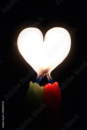 Two burning candles with a flame in the form of a heart on a black background