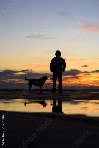 Silhouette of man with his dog at sunset on background