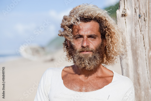 Robinson Crusoe. Portrait of curly-bearded man on the beah with a ship wreckage on the background. photo