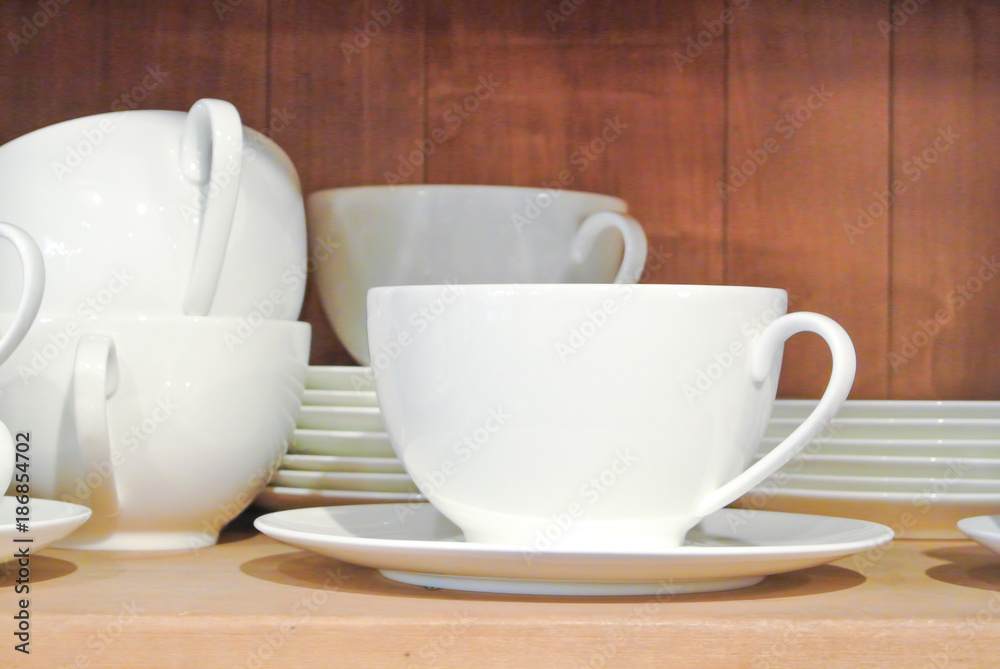 Bright white dishes, plates and cups standing on brown wooden shelf. Concept of buying choosing new dishes for house home, interior indoor decoration o for gifts. Clean ordered dishes in store.