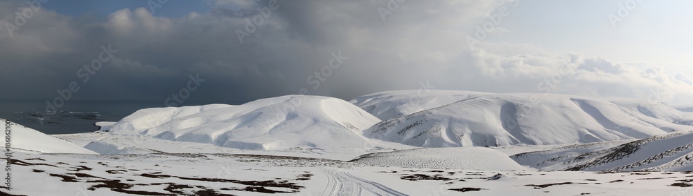 panorama of the winter tundra floodplain of the river flowing between the snow-covered hills to the ocean