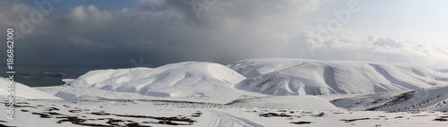 panorama of the winter tundra floodplain of the river flowing between the snow-covered hills to the ocean