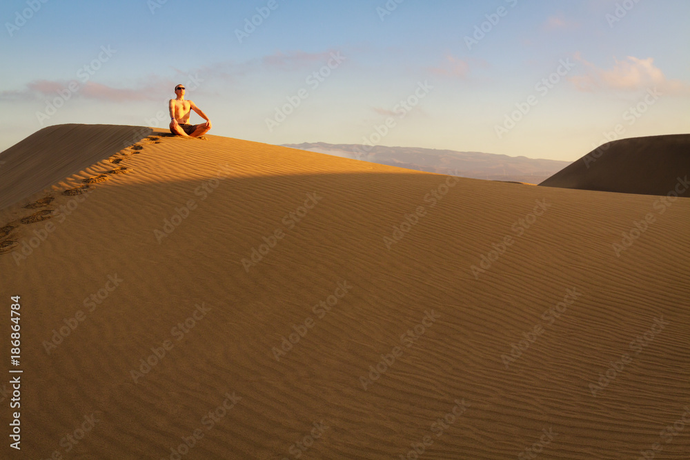 Man sitting and relaxing on sand dunes by the sunrise, in Maspalomas on Gran Canaria.
