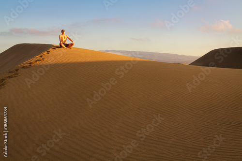 Man sitting and relaxing on sand dunes by the sunrise  in Maspalomas on Gran Canaria.