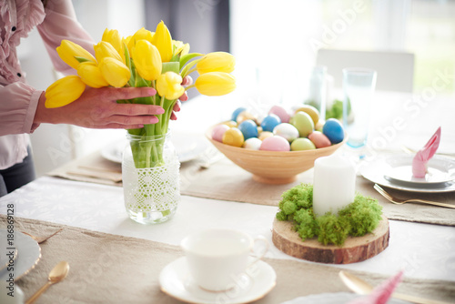 Hands of woman arranging yellow tulips at easter dining table photo