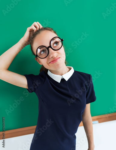Nerdy student in standing thinking and looking towards. Photo of indecisive girl wearing glasses near green board. Creative concept
