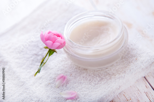 Spa setting with pot of moisturizing cream beautiful pink roses and rose oil on white background top view