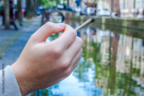 Canvas Print hand holding a cannabis joint on a canal in Amsterdam