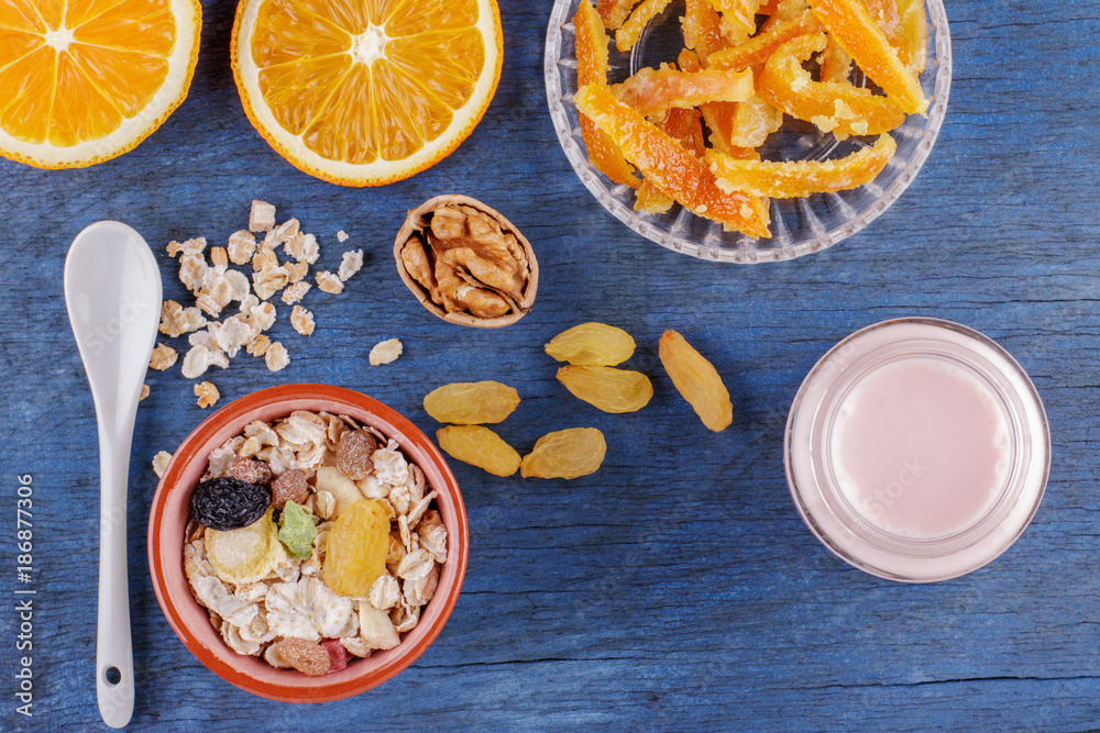Healthy breakfast. Ceramic bowl with oat flakes, dried fruits, nuts, candied fruit, orange on wood background