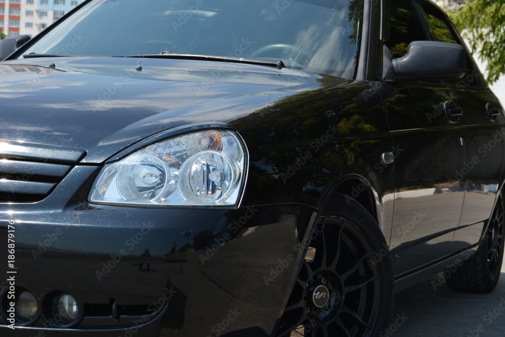 Black shiny car. The headlight and the side of the car. Car on black cast wheels.