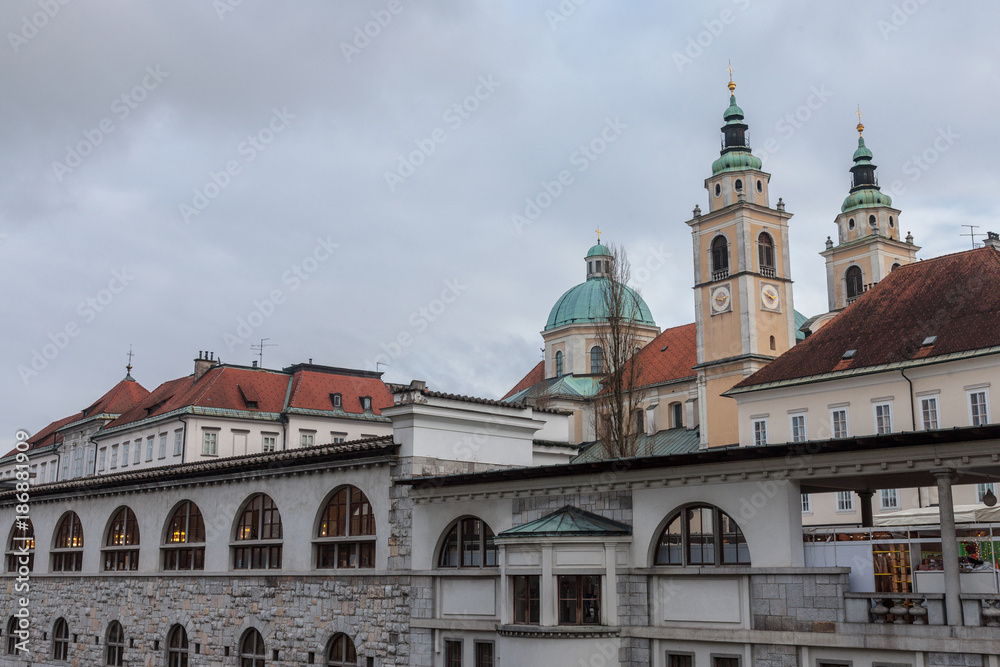 Central Market of Ljubljana, capital city of Slovenia, taken during a cloudy rainy day, with the Ljubljanica river on foreground and the Ljubljana Cathedral (Saint Nicholas Church) in the background.