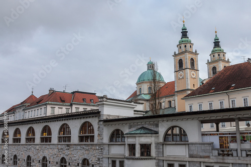 Central Market of Ljubljana, capital city of Slovenia, taken during a cloudy rainy day, with the Ljubljanica river on foreground and the Ljubljana Cathedral (Saint Nicholas Church) in the background.