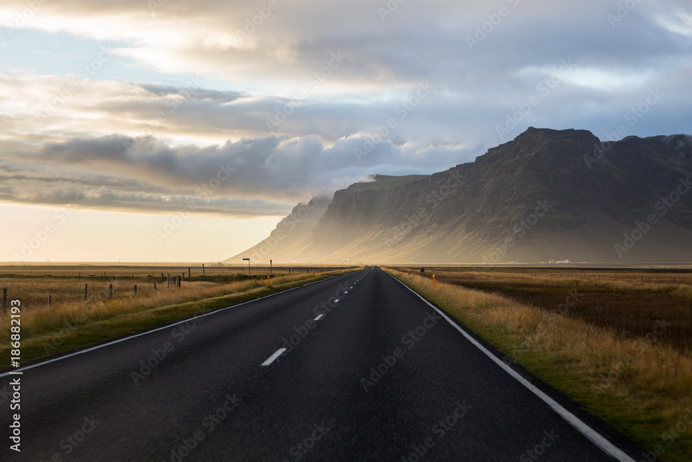 Photo of a long stretch of road with a beautiful breathtaking scenery of the mountains and the sunset