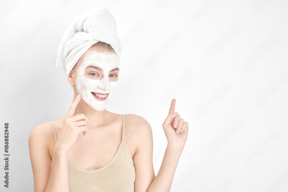 Skin care. A young woman in a mask and a towel on his head pointing finger on white background