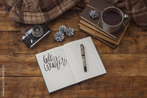 A beautiful composition on a winter theme with a mug of hot tea, a blanket, a diary and a pen. Added the text Hello winter.