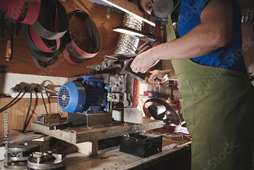 Making of a knife. Master sharpens a blade on the machine closeup in the Studio