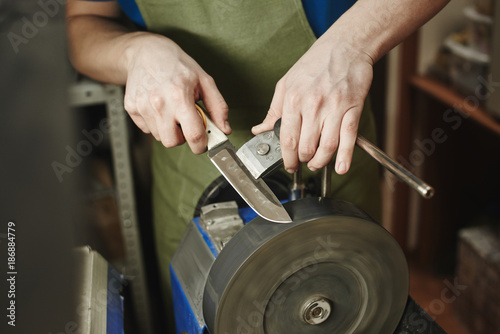 Making of a knife. Master sharpens a blade on the machine closeup in the Studio