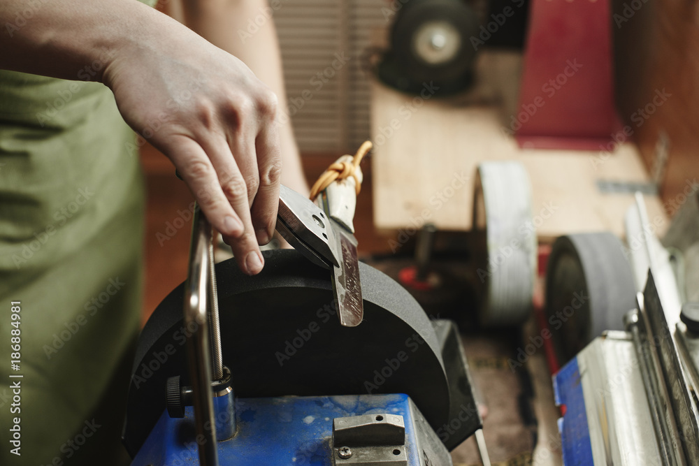 Making of a knife. Master sharpens a blade on the machine closeup in the Studio Making of a knife. Master sharpens a blade on the machine closeup in the Studio